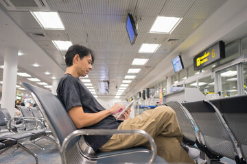 business concept with asian man sit on chair and work with tablet in airport