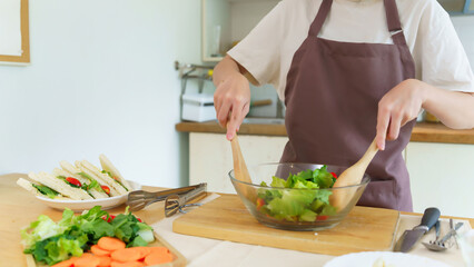 Asian women using wooden spoon to mixing ingredients and slices of fresh vegetable in the glass...