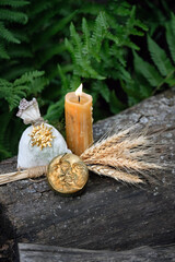 Burning candle, witch bag, wheat ears and symbolic moon amulet in forest, natural background. Witchcraft, magic practice. esoteric spiritual ritual for for Lammas, Lughnasadh.