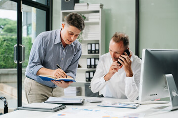 Two business workers talking on the smartphone and using laptop