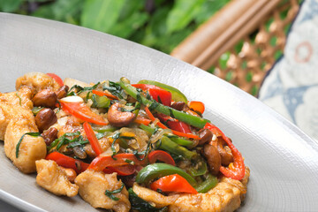 A plate of stir-fried chicken with an assortment of colorful vegetables, including bell peppers, mushrooms, and bright green herbs, garnished with roasted nuts.