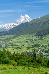 Fototapeta premium Mountains covered with forest and bushes. Villages in the valley. Light Clouds Above the snow capped peak of Mount Ushba