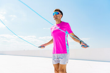 Man in vibrant sportswear joyfully jumps rope under a clear sky, embodying fitness and vitality.