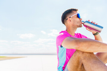 Man in athletic attire sips water under the bright sky, embodying the essence of active relaxation.