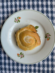 Fresh homemade cinnamon roll on a decorative plate with a checkered tablecloth background