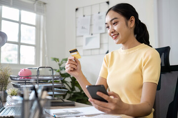 Young Woman Using Credit Card and Mobile Phone for Online Shopping in Modern Home Office Setting