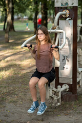 Beautiful teenage girl actively engaged in sports on outdoor exercise machines. Sports. Healthy...