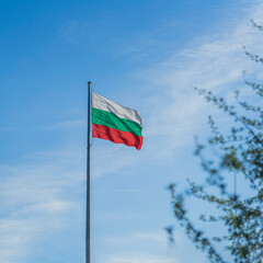 National flag of Bulgaria on flagpole in front of blue sky with clouds