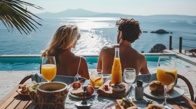 back view of the couple enjoying breakfast on a hotel terrace with a beautiful ocean view, summer vacation destination for couples