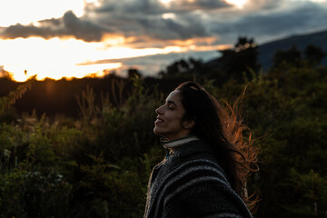 Multiracial Latino young woman in poncho taking a selfie at sunset in the Ecuadorian Andes