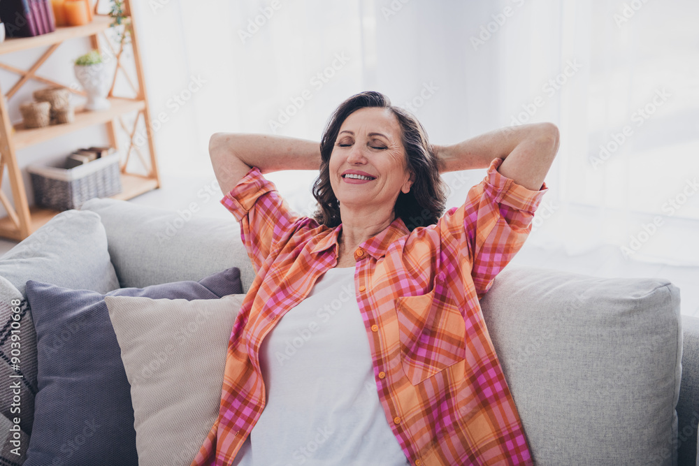 Wall mural Photo of pretty cheerful lady wear plaid shirt smiling arms behind head indoors room home house