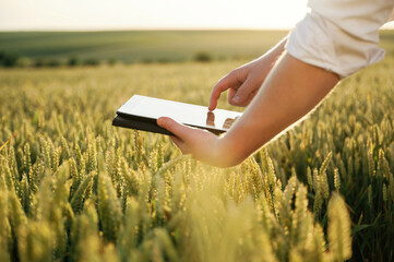 Black digital tablet. Man in white shirt is on the agricultural field