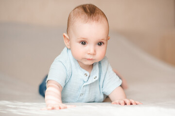 Cute infant baby boy 4-5 months old crawling in bed wearing blue stylish onesie close up. Childhood.