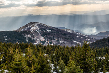Awesome winter landscape in the mountains with rays of sun piercing through the clouds to the mountain trees.