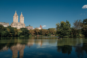 View of modern tall buildings, trees and blue lake in New York City's Central Park, Manhattan on a summer day