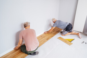 Father and adult son installing flooring in new Home by their own. Doing measurements, calculating for vinyl laminate and skirting. DIY, Do it yourself. Home renovation, improvement, refurbishment.