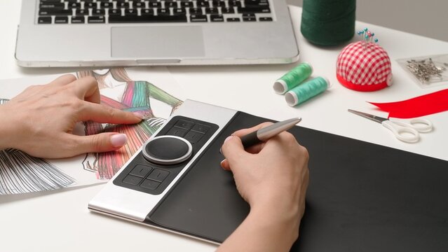 Woman fashion designer works on digital graphic tablet with stylus, hand drawing women clothes project illustration. Creativity and modern technology.
