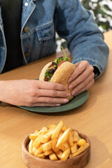 Woman eats delicious hamburger with french fries at table