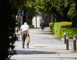 真夏の昼の住宅街で歩く一人のシニア男性の姿