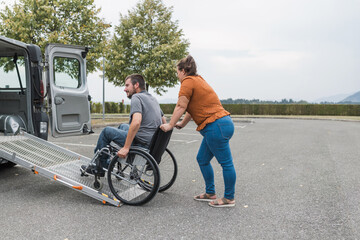 Female assistant helping a male person in wheelchair with transport using accessible vehicle van...
