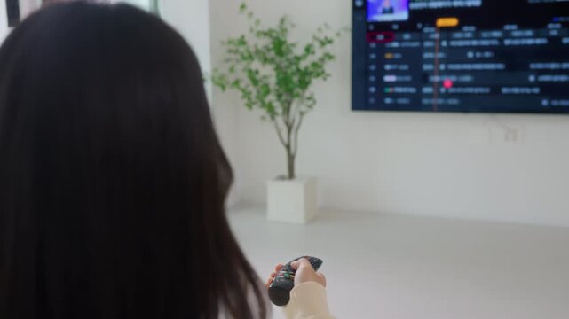 Woman operating television with remote control in bright living room
