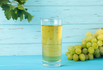 Glass of grape juice on blue wooden background. Green grape