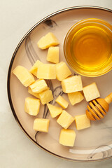 A piece of Parmesan cheese with honey on plate on light background.