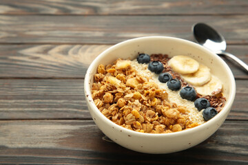 Oat raisin granola with fresh summer berries in a bowl on brown wooden background. Concept of healthy breakfast food, clean eating, dieting