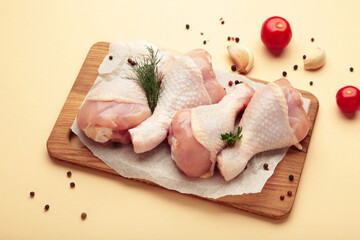Raw chicken drumsticks with spices on cutting board on beige background. Top view. Free space for your text.