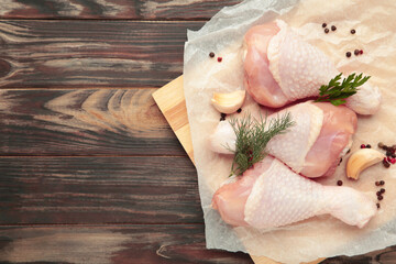 Raw chicken drumsticks with spices on brown wooden background. Top view. Free space for your text.