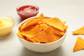 Nachos in bowl with ketchup and cheese sause on light background. Mexican dish. Top view