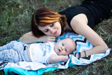 Young mother and newborn baby boy child lies with blanket outdoors in summer on grass