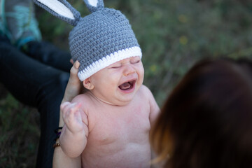 Newborn baby screaming, young mother holding her baby boy in hands, outdoors in summer in sun rays