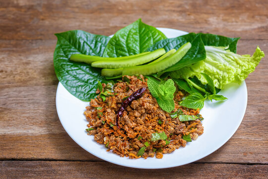 Larb Ped Spicy Minced Duck Salad on wood table with fresh vegetables. Thai local food recipe Larb Ped delicious menu containing ingredients of many Thai herbs.