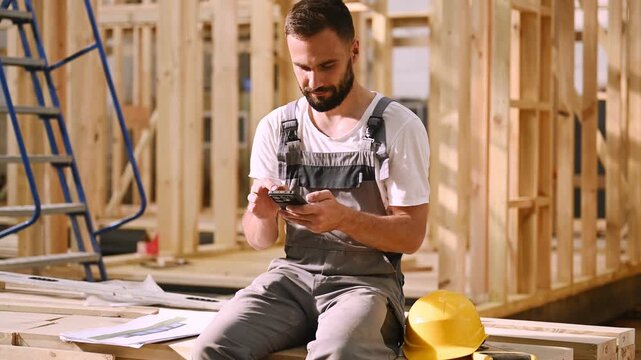 Taking a rest, sitting with smartphone. Industrial worker in wooden warehouse.