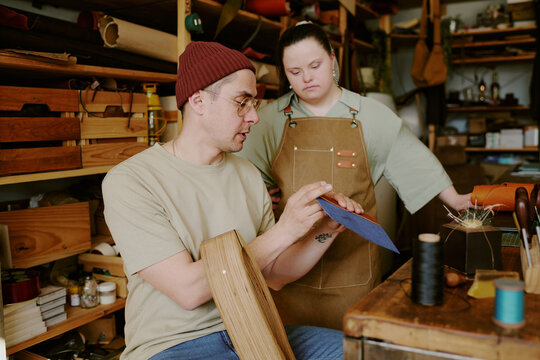 Male tailor showing done leather detail to his female intern with down syndrome