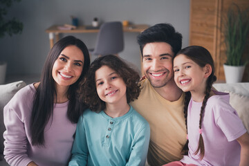 Photo of positive good mood parents children dressed casual clothes smiling hugging indoors house apartment room