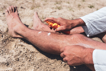 Man applying sunscreen to his legs on the beach