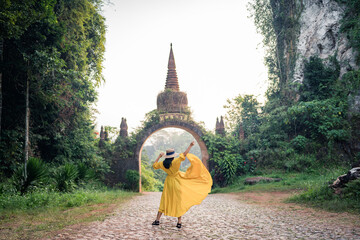 Asian female tourist in yellow dress and hat at The large ancient pagoda arch is beautiful, Khao Na Nai Luang Dharma Park, Surat Thani, Thailand.