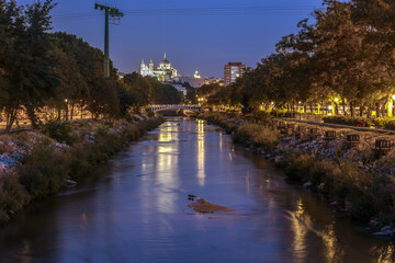 Fototapeta premium Panoramic view of Madrid at night, during the blue hour, with the Almudena cathedral in the background, over the Reina Victoria bridge, which crosses the Manzanares river.