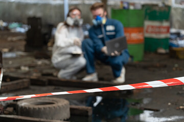 emergency pollution factory concept. engineers wearing mechanic jumpsuits and ppe and gas masks inspect oil on the factory floor.