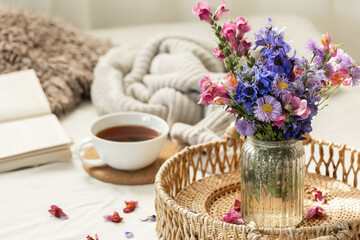 Cup of tea, a bouquet of wildflowers, book and knitted element.