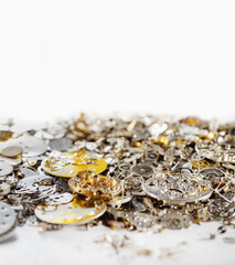 Gears, clock faces and metal parts of internal mechanism of the watch lie in heap on white background.