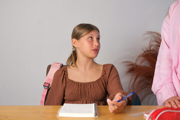 Teenage girl sitting at table doing homework, mother standing next to her helping her. Mothers support during learning. Back to school. Secondary education.