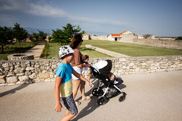 Obraz premium A family walking at a historical site with children and a stroller on a sunny day in Nin, Croatia.