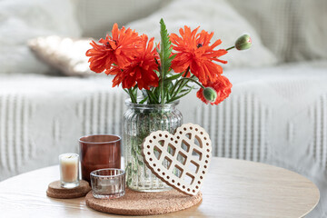 A minimalistic composition with red poppy flowers in a vase and candles at home.