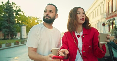 A brunette girl in a red jacket helps a guy in a white T-shirt find his way using Internet maps on the street in an unfamiliar area in the city
