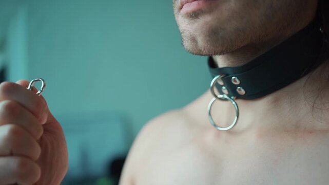 sexy man with naked torso holding bdsm leather collar with silver chain, fetish and sex role play game with toys, male slave dominance and submission concept