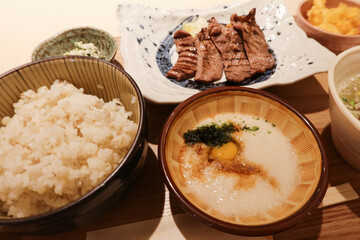 close up of Japanese meal set containing grilled ox beef tongue with granted yam and raw egg yolk and rice on a wooden tray