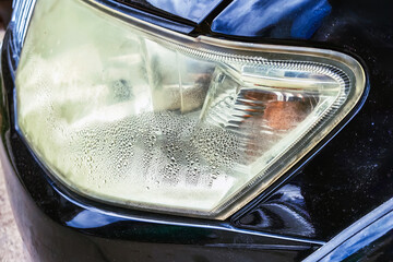 Water vapor in car headlights. Condensation in headlights. Car lamp with water inside. Fogged up headlight lenses. Moisture inside the car headlight. Water droplets condensation inside car headlamp. © JinnaritT